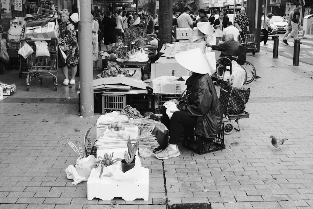 A street vendor sits among products and pedestrians.