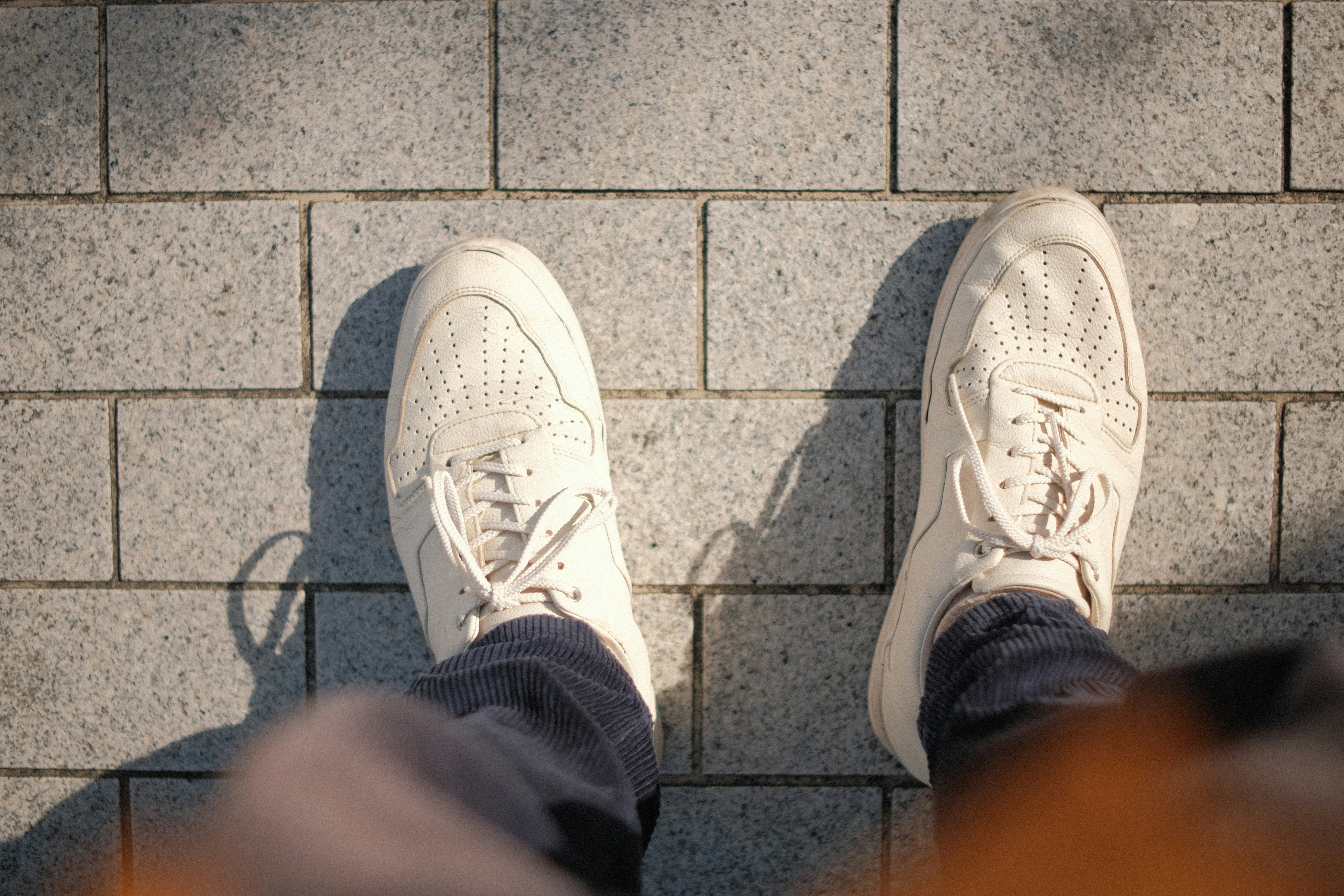 a person wearing white tennis shoes standing next to a brick wall